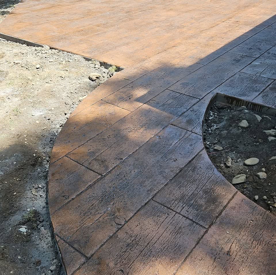 Curved stamped concrete walkway with a wood-plank pattern joining a stamped patio